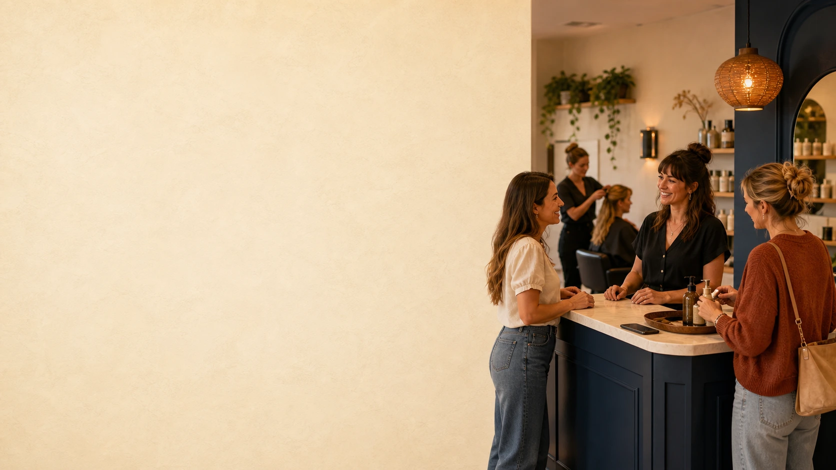 A salon owner greeting a client at reception while another client receives service nearby